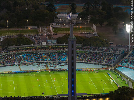 Vista aérea de la bandera uruguaya flameando en lo alto de la torre de los homenajes del Estadio Centenario mientras se juega un match amistoso nocturno - Departamento de Montevideo - URUGUAY. Foto No. 78444