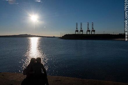 Silueta de una pareja sentada en la escollera Sarandí en contraste con el reflejo del sol en el río - Departamento de Montevideo - URUGUAY. Foto No. 79210